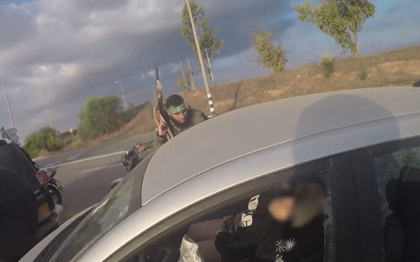 a hamas terrorist riding on the back of a car, wearing a green headband